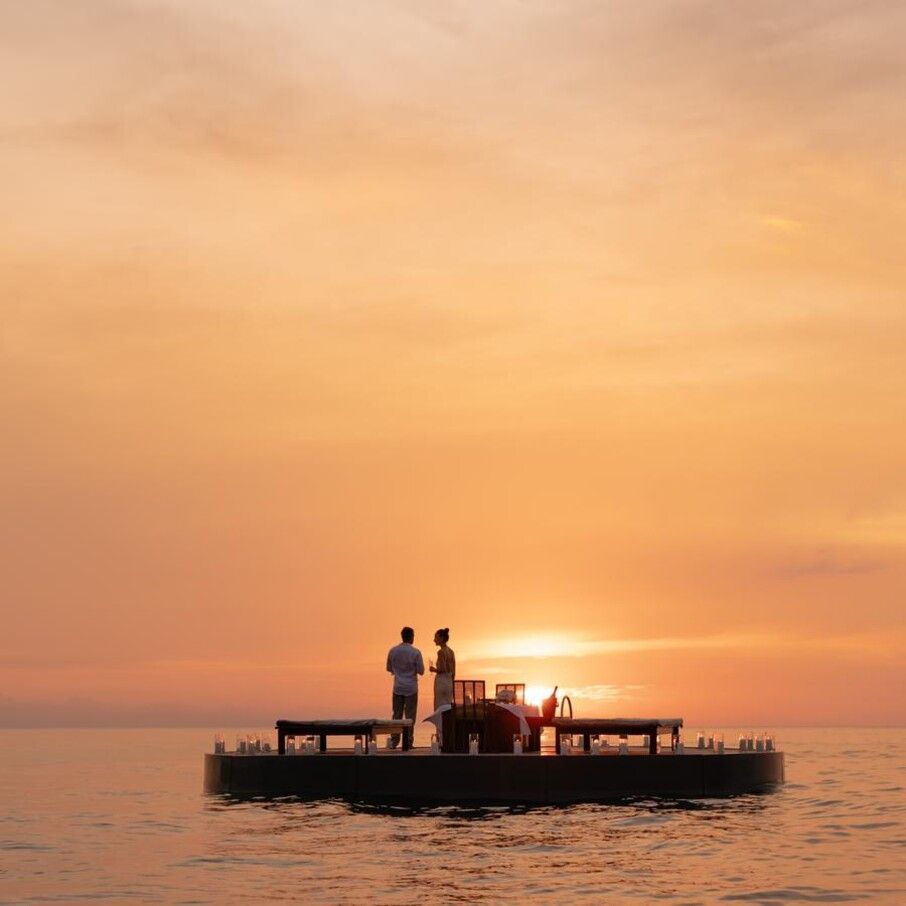 Couple watching sunset from a floating platform in the ocean, orange sky. The Amanpuri, Phuket