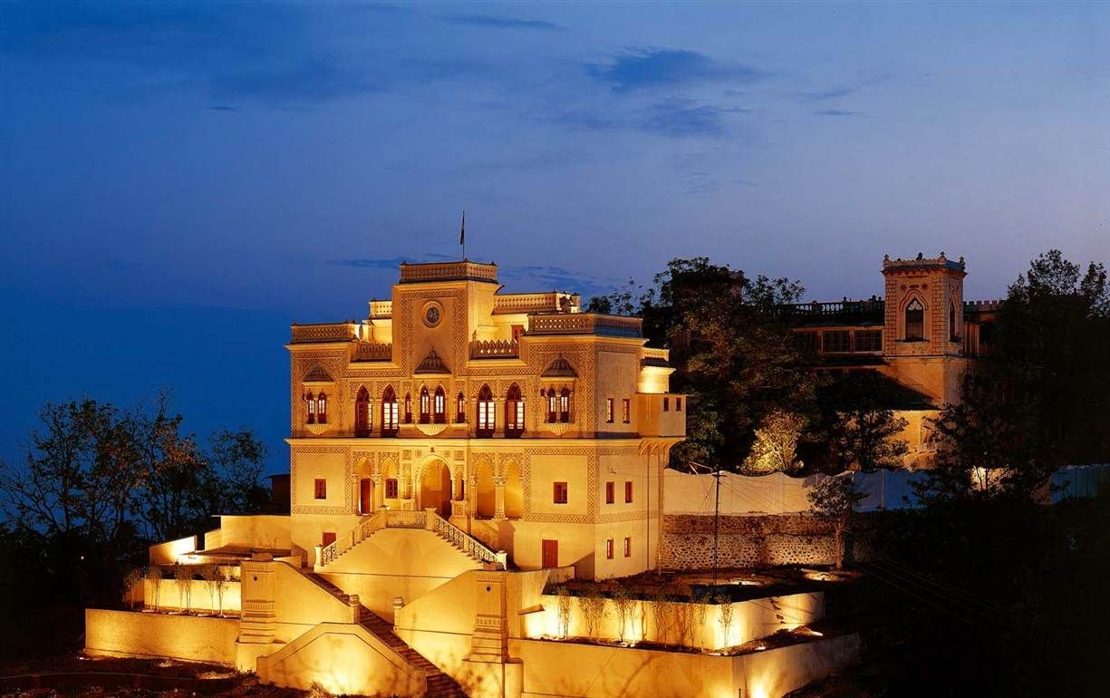 Ananda in the Himalayas A grand, illuminated stone building at dusk, possibly a palace or hotel, with steps leading up to the entrance.