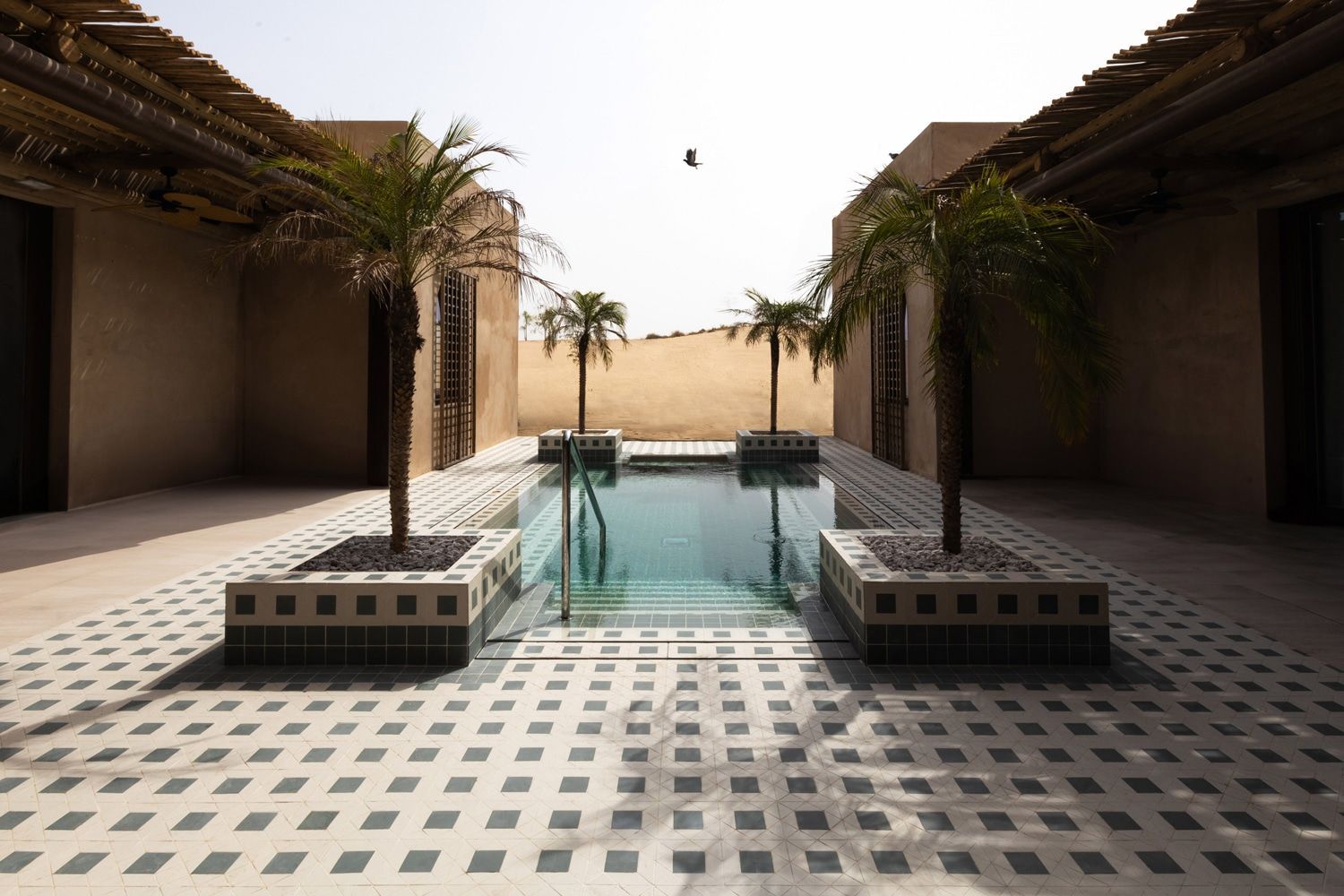 Pool area with palm trees, beige walls, and tiled flooring against a desert backdrop.