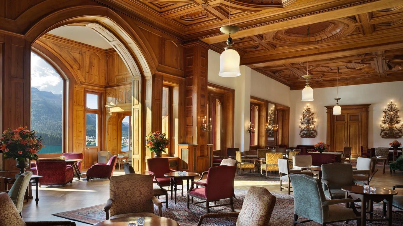 Elegant wooden-paneled interior with arched windows, tables, chairs, and decorative ceiling; light streams in. Badrutt’s Palace Hotel experience