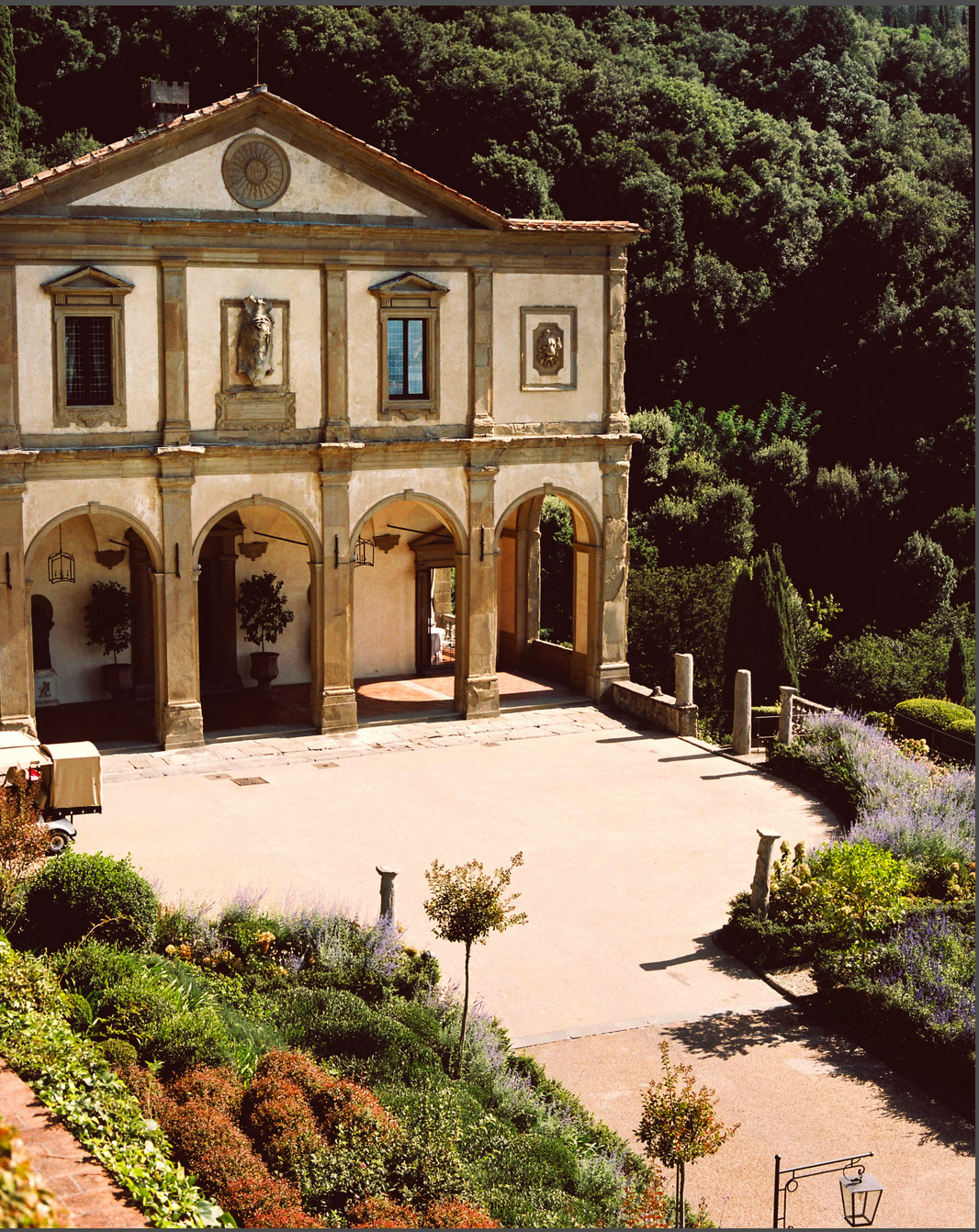 A classical Italian villa with arches, windows, and a surrounding garden in a lush, green setting. Belmond Villa San Michele
