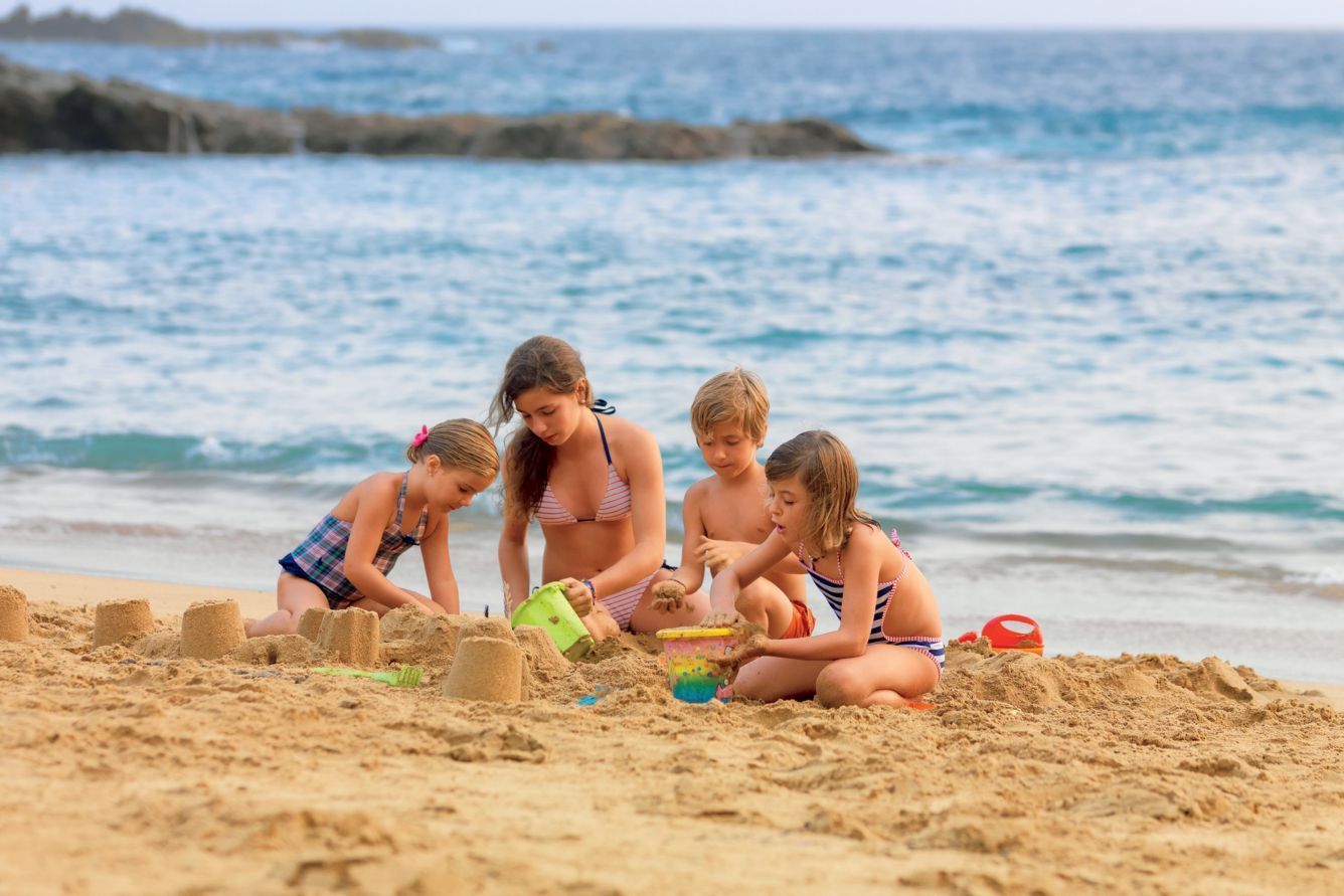 Children building sandcastles on a sandy beach near the ocean.