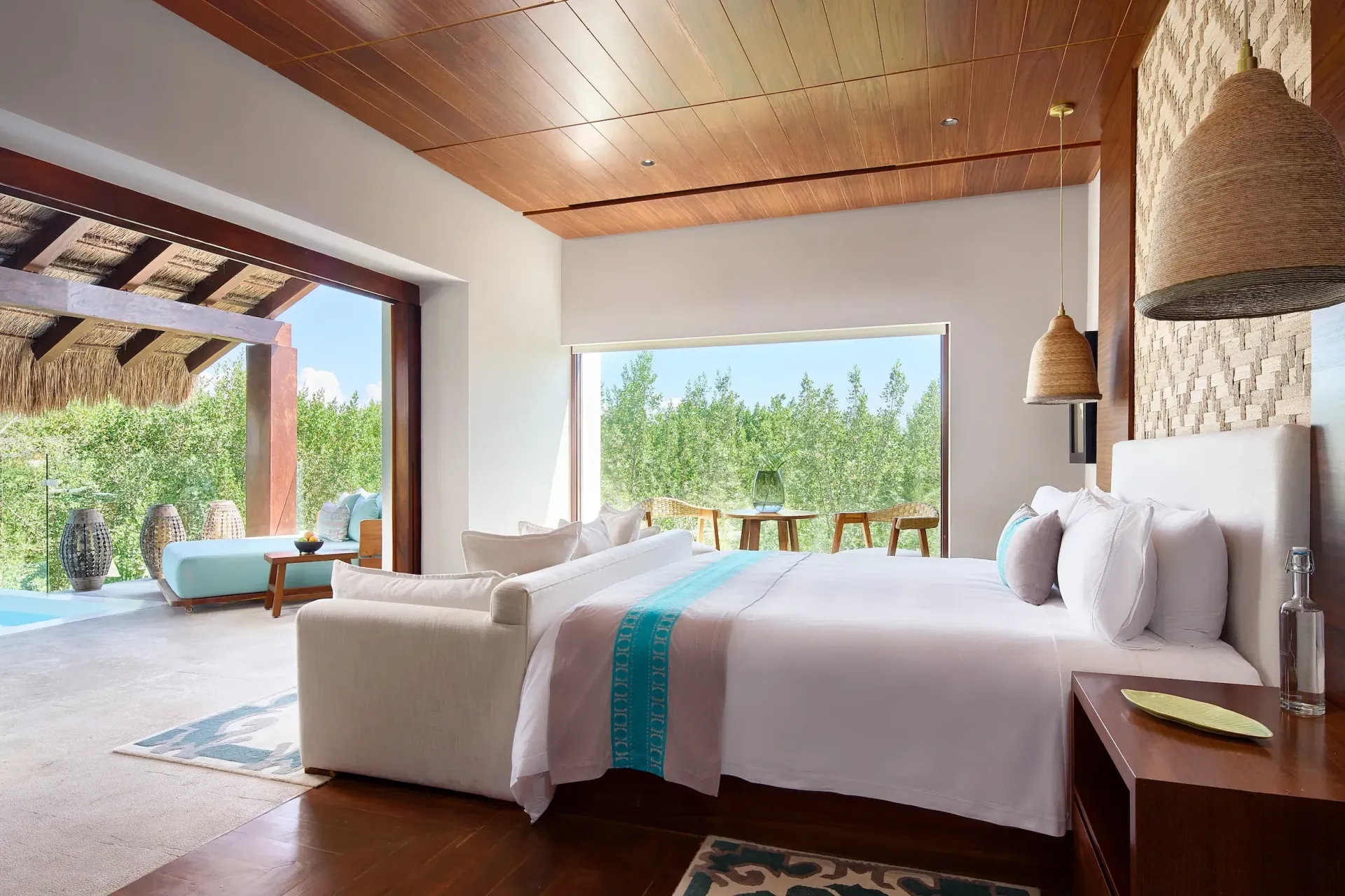 A luxury resort bedroom with a large bed, textured ceiling, woven lighting, and an open terrace overlooking lush greenery. Chablé Maroma