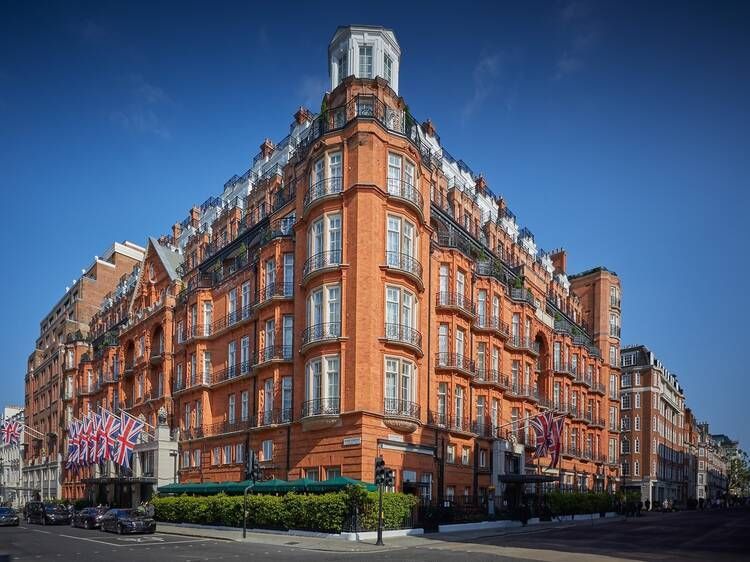 Red brick hotel on a corner with Union Jack flags, sunny day. The Dorchester (Park Lane)