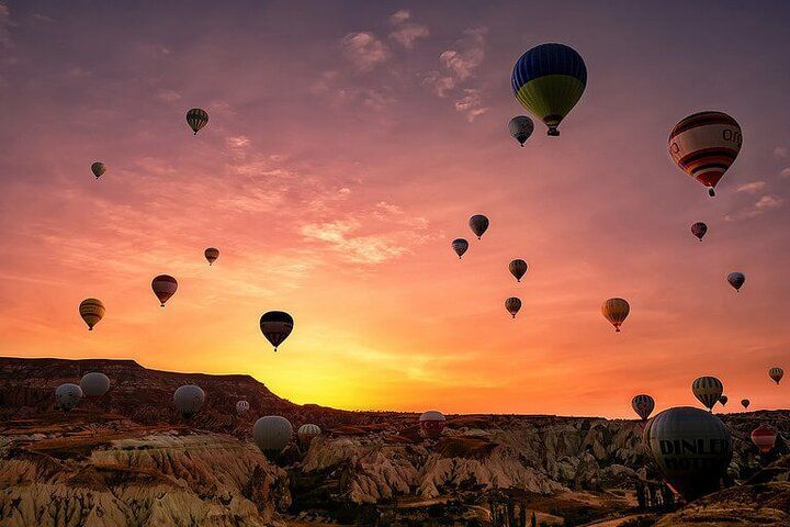Hot air balloons ascend at sunset over a unique rock formation landscape.