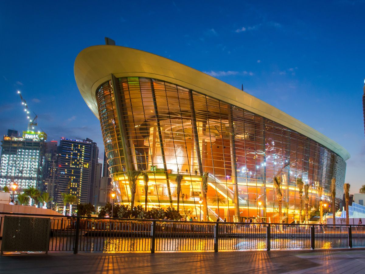 Dubai Opera House at night, illuminated, modern glass and gold building reflecting in water.
