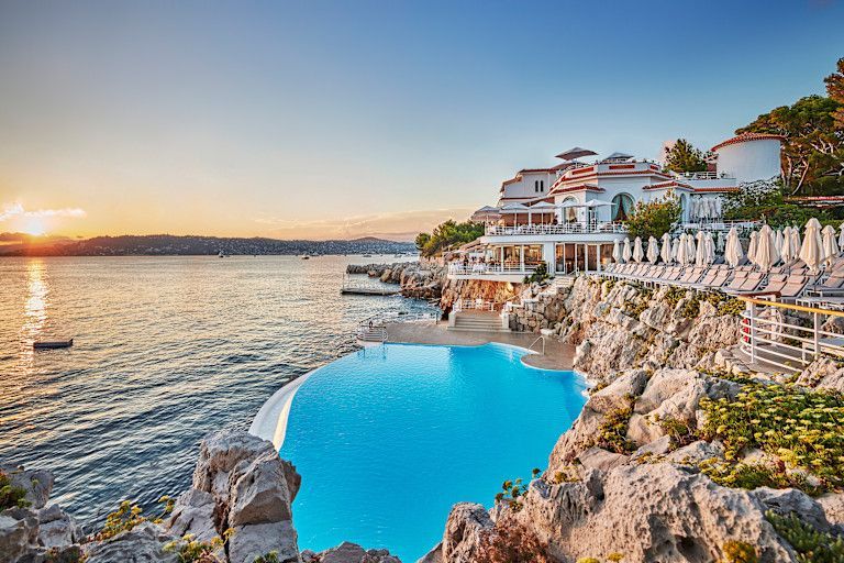 Luxury hotel on rocky coast with infinity pool overlooking the ocean at sunset. Hotel du Cap-Eden-Roc