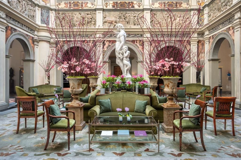 An ornate room with couches, chairs, and flower arrangements surrounding a marble statue. Four Seasons Hotel Firenze