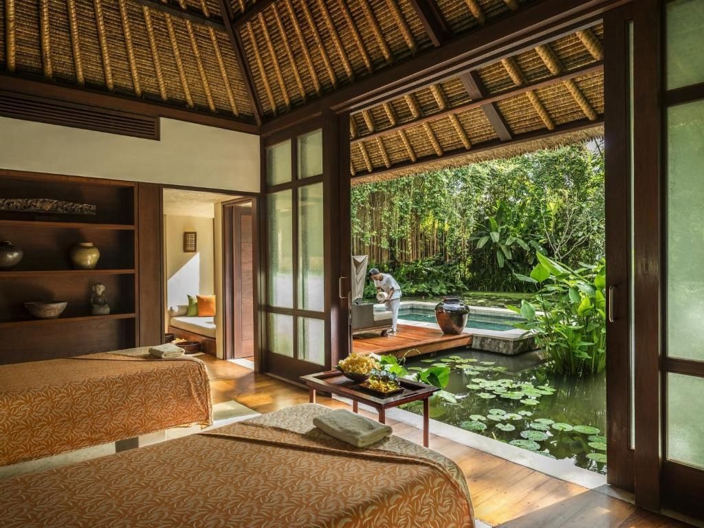 Spa room with massage beds, open doors to a garden with water, lush greenery, thatched roof. Four Seasons Resort Bali