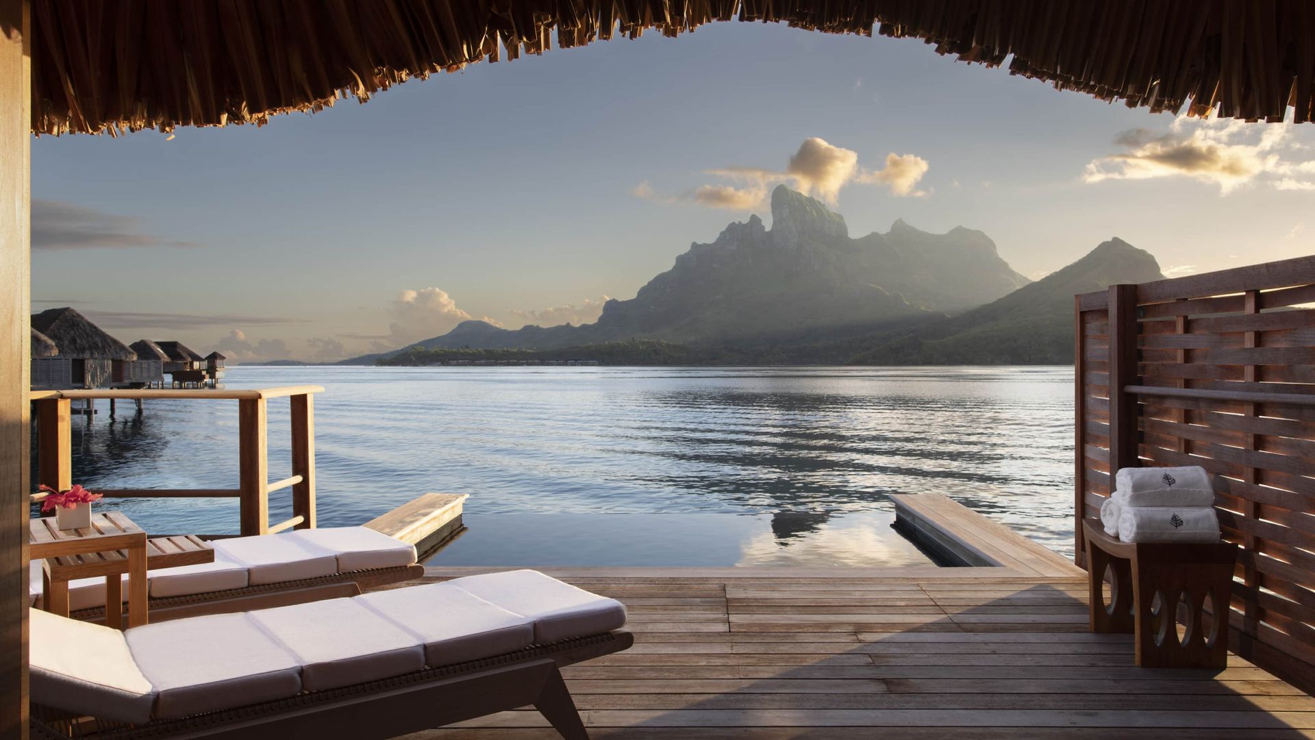 Overwater bungalow deck with lounge chairs facing calm water and a mountain range. Four Seasons Resort, Bora Bora