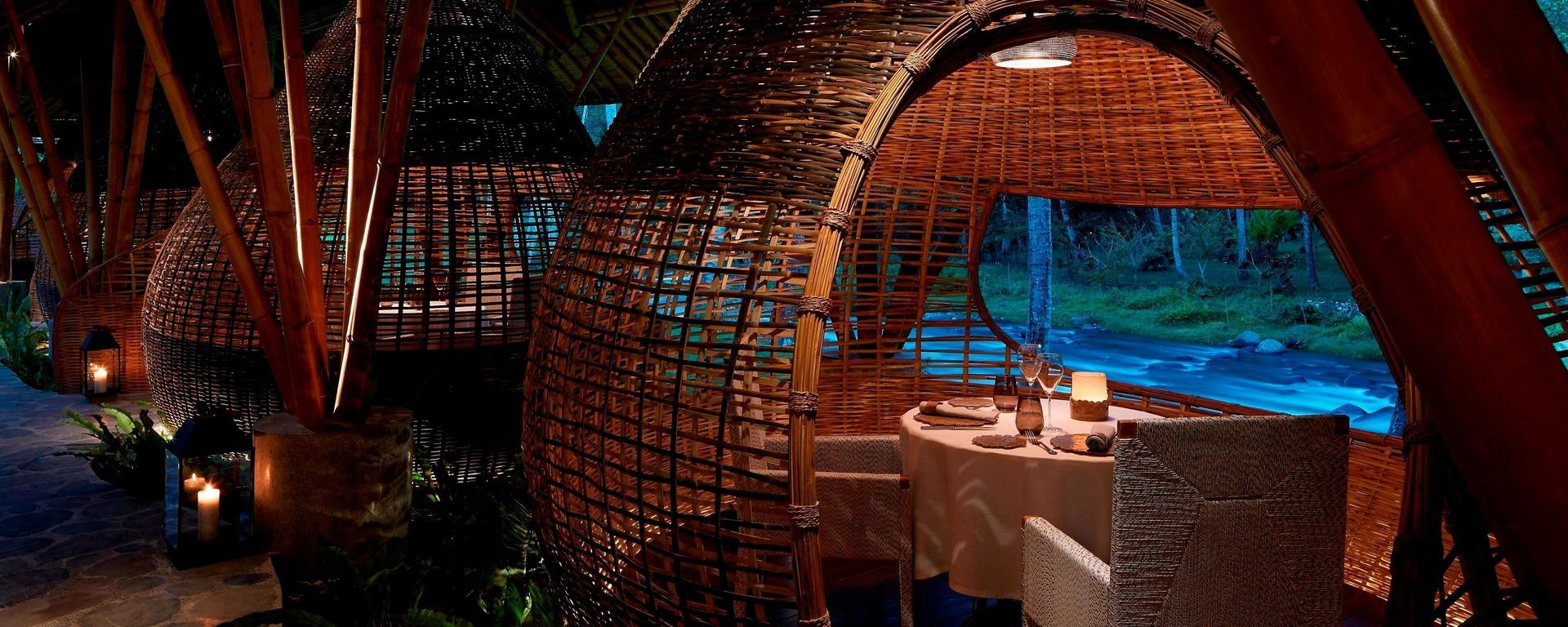 Cozy, organic-looking restaurant interior with wooden walls and ceiling. Table set, overlooking a river.