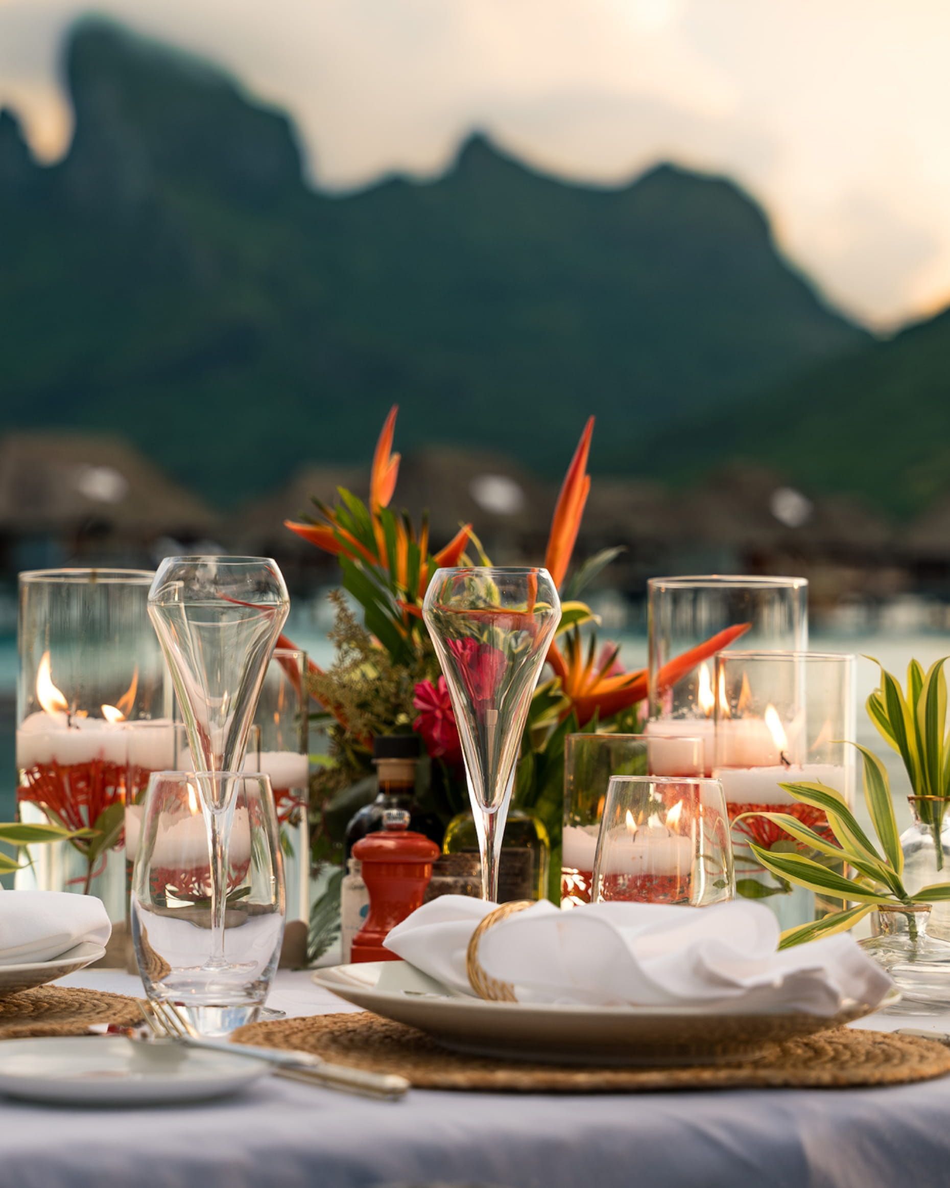 Elegant table setting with floral arrangement, champagne, and candles overlooking water and mountains. Four Seasons Resort Bora Bora