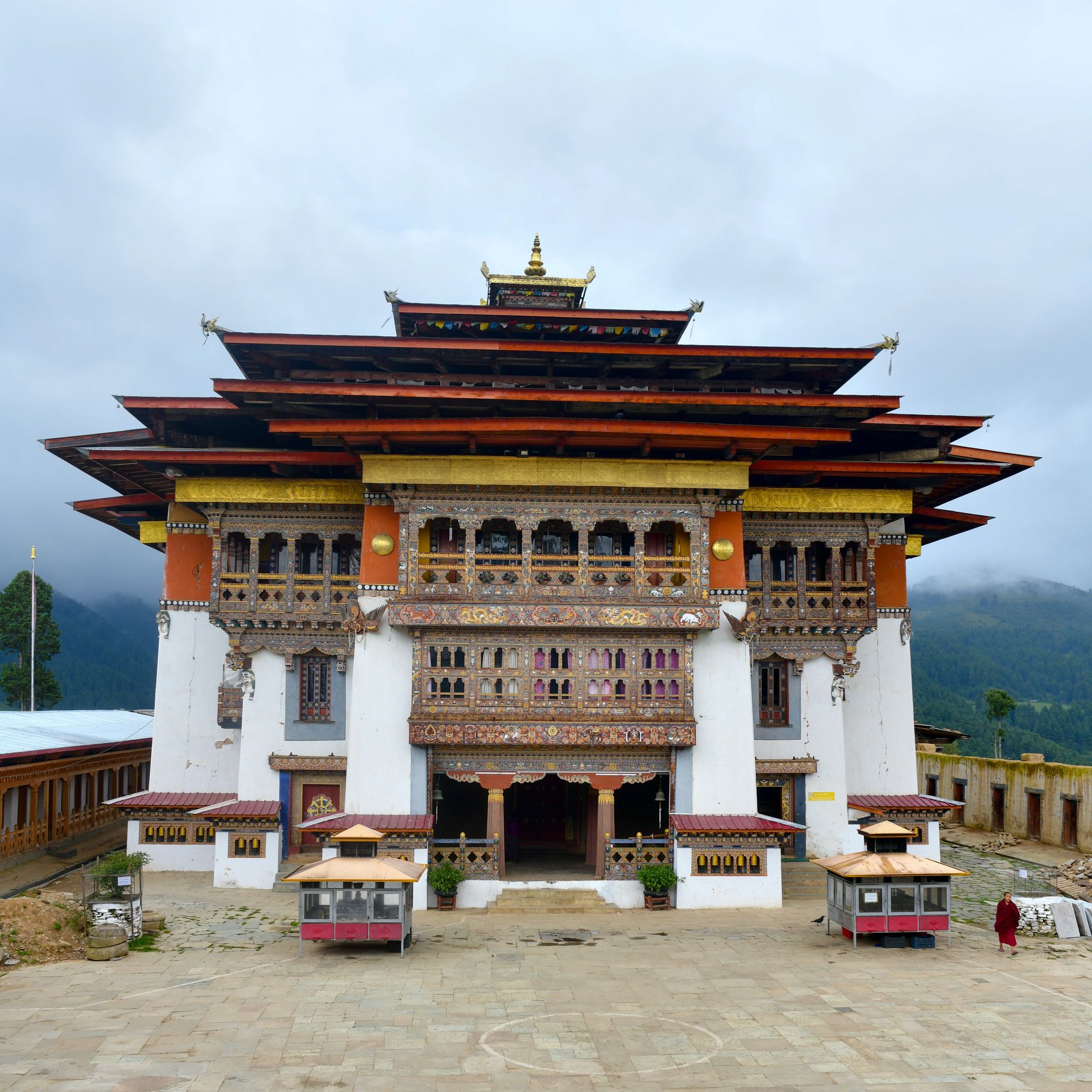 Whitewashed Bhutanese temple with red-brown tiered roof and ornate wooden balconies, against a cloudy sky. Gangtey / Phobjikha Valley