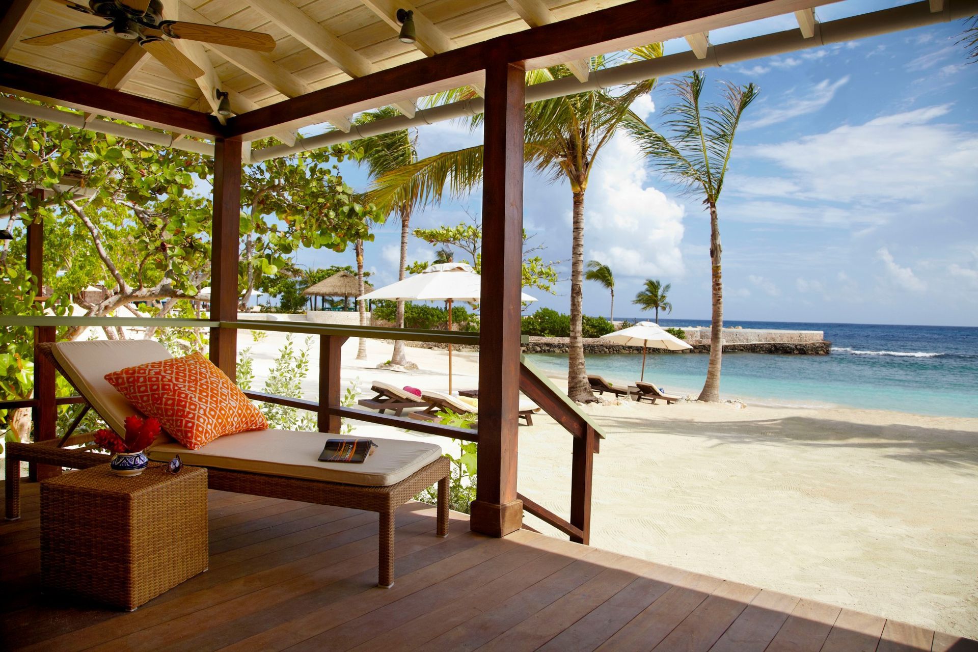 Beachfront veranda with a lounge chair, ocean view, and palm trees. GoldenEye Lagoon Villas – Jamaica
