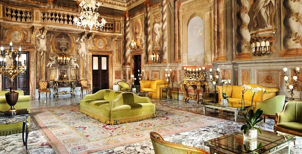 Opulent, gold-toned room with ornate carvings, chandeliers, and green seating on patterned flooring.Grand Hotel Continental Siena