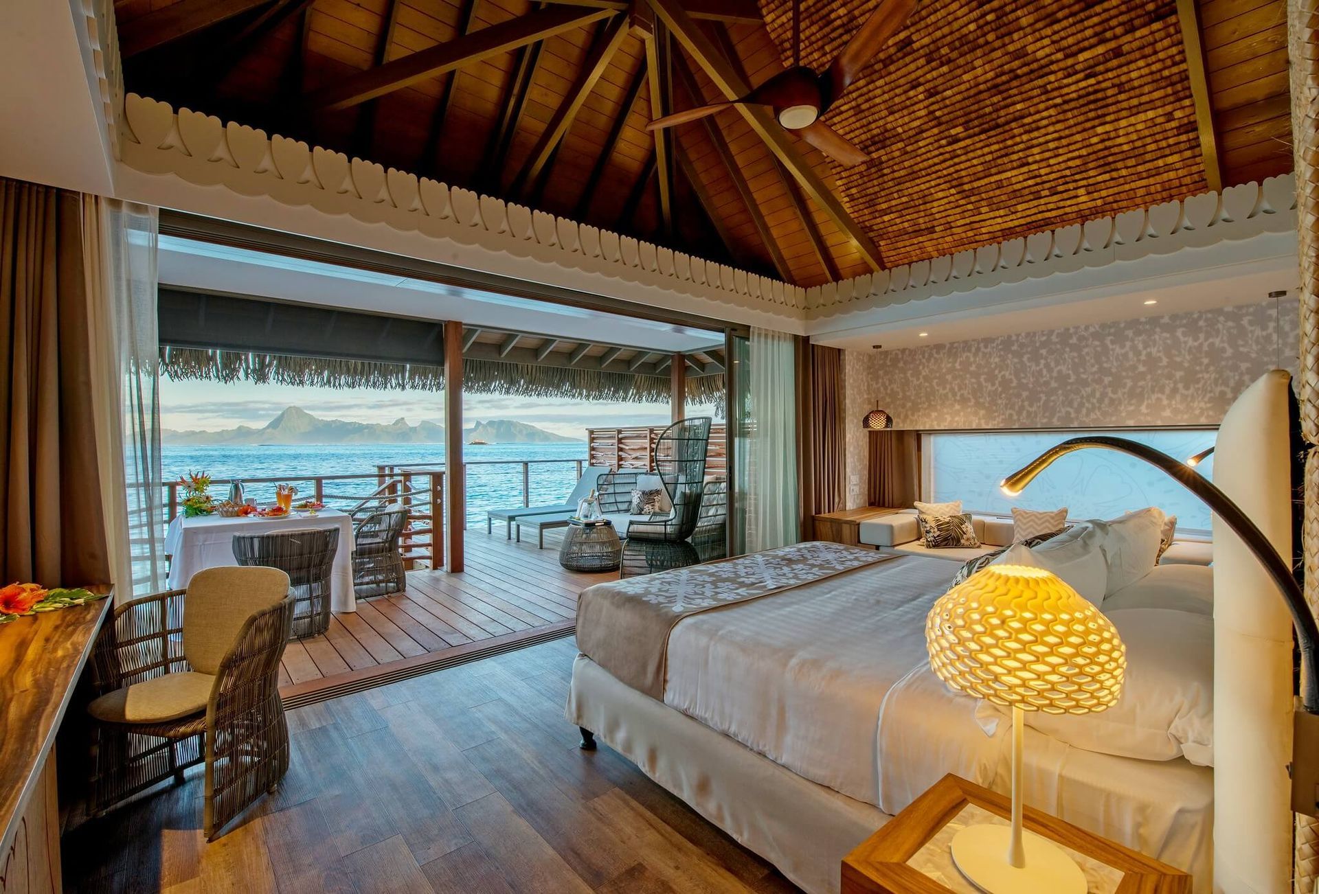 A luxurious bedroom in an overwater bungalow with a large bed, wicker furniture, and an open terrace overlooking the sea. Room  InterContinental, Tahiti
