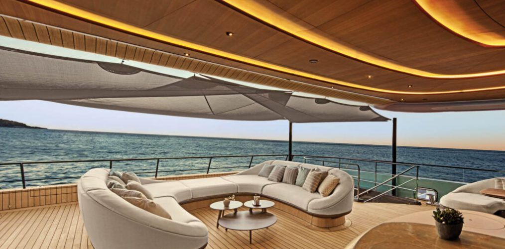 A luxury yacht deck with curved beige sofa, small tables, and a view of the sea.