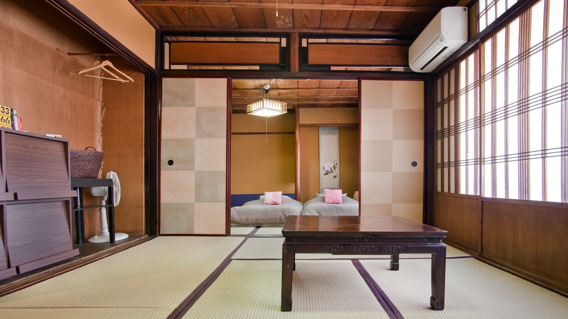 Japanese-style room with sliding doors, tatami mats, and a low table, leading to a bedroom with two beds. JAPAN RYOKANS