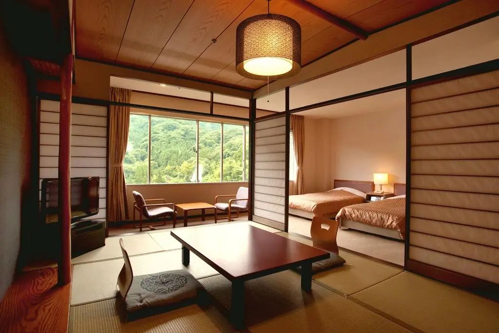 Japanese-style hotel room with tatami mats, low table, and sliding doors. Twin beds in adjacent room. JAPAN RYOKANS