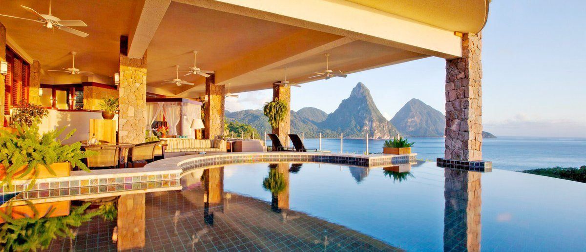 A luxury open-air patio with an infinity pool overlooking the Piton mountains and the Caribbean Sea at sunset. Jade Mountain, St Lucia