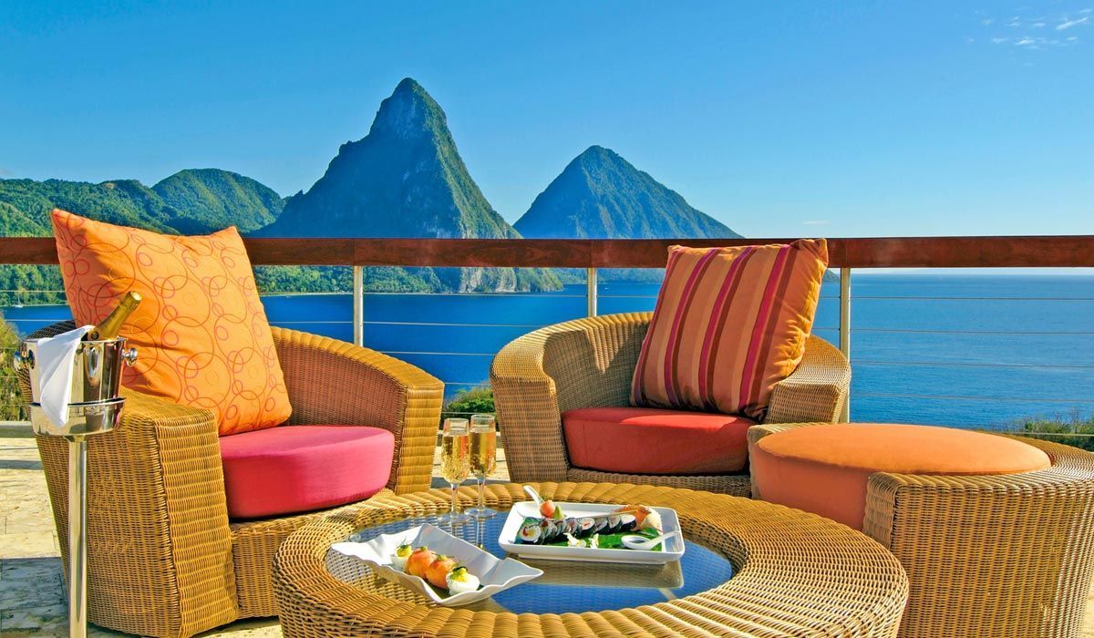 Wicker patio furniture with colorful cushions overlooks the Pitons mountains and the Caribbean Sea in St. Lucia. Jade Mountain, St Lucia