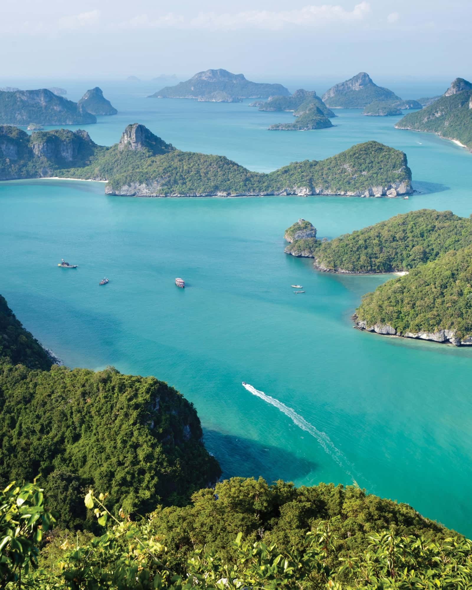 Turquoise sea with green, hilly islands; boats dot the water, a sunny, scenic vista.