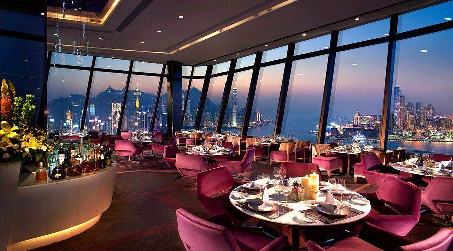 Upscale restaurant with city view, tables, pink chairs, bar, and large windows.