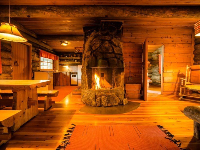Cozy cabin interior with a lit fireplace, wooden beams, a table, and a hallway to another room.