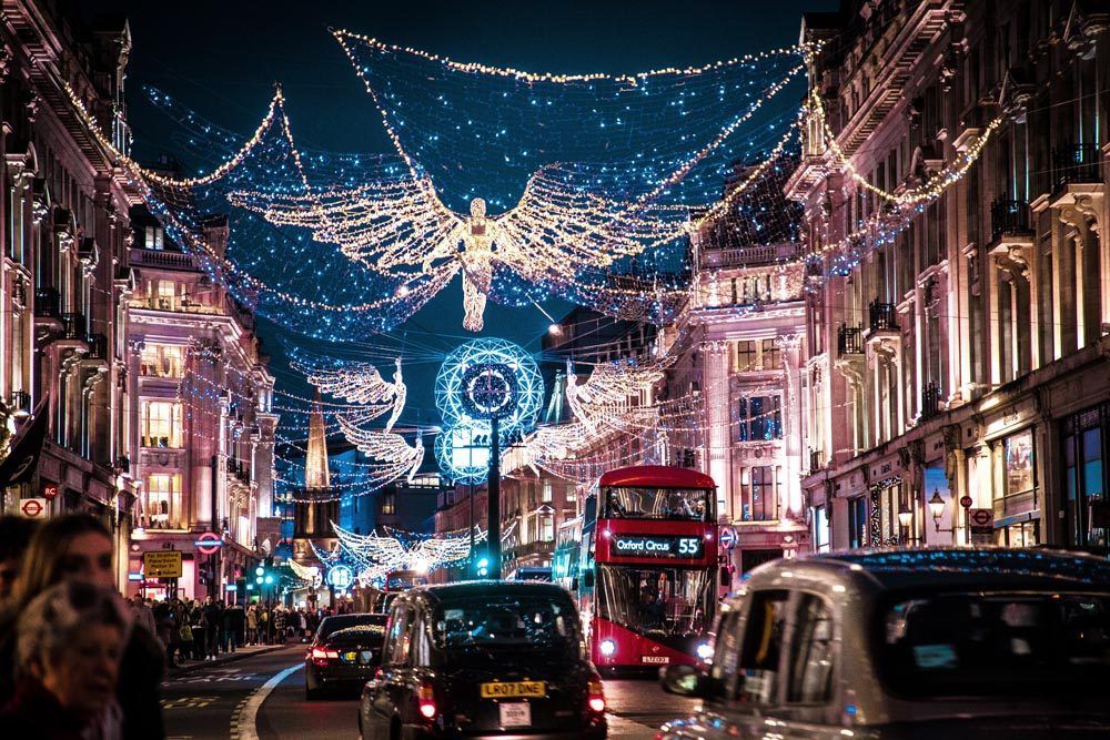 Regent Street, London decorated with Christmas lights at night, featuring a red double-decker bus.