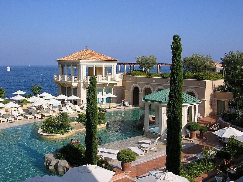 Luxury resort with pool and ocean view, featuring beige buildings, white umbrellas, and clear blue water.