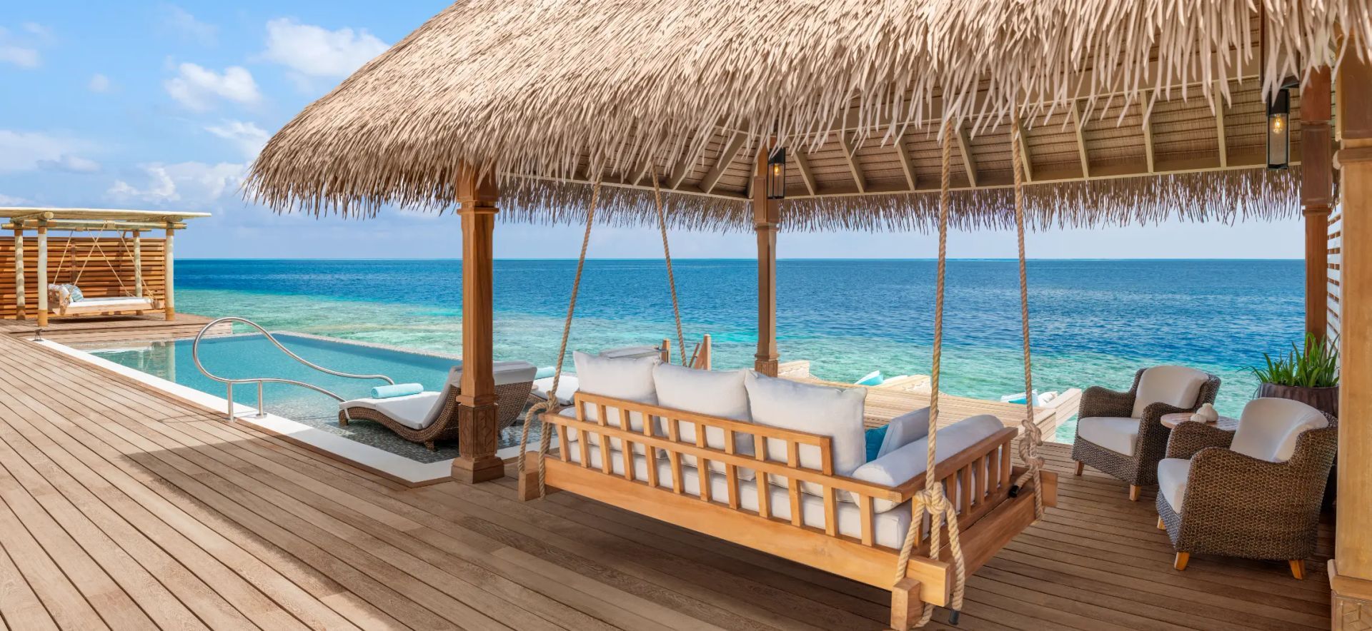 Tropical deck with pool, ocean view, swing bed, and lounge chairs under a thatched roof.