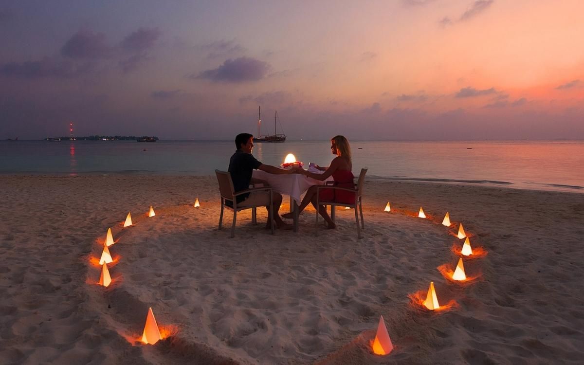 Couple at candlelit beach dinner at sunset.