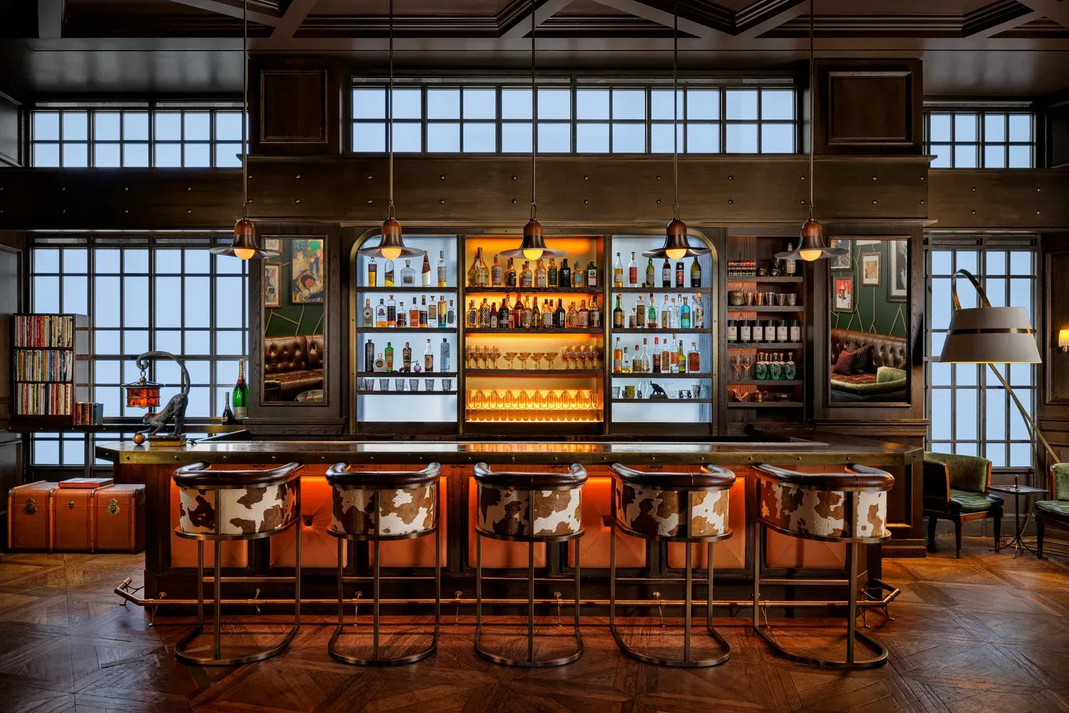 Mandarin Oriental, New York – Columbus Circle A luxurious bar with cowhide barstools, a well-stocked back bar, and large windows overlooking a cityscape.