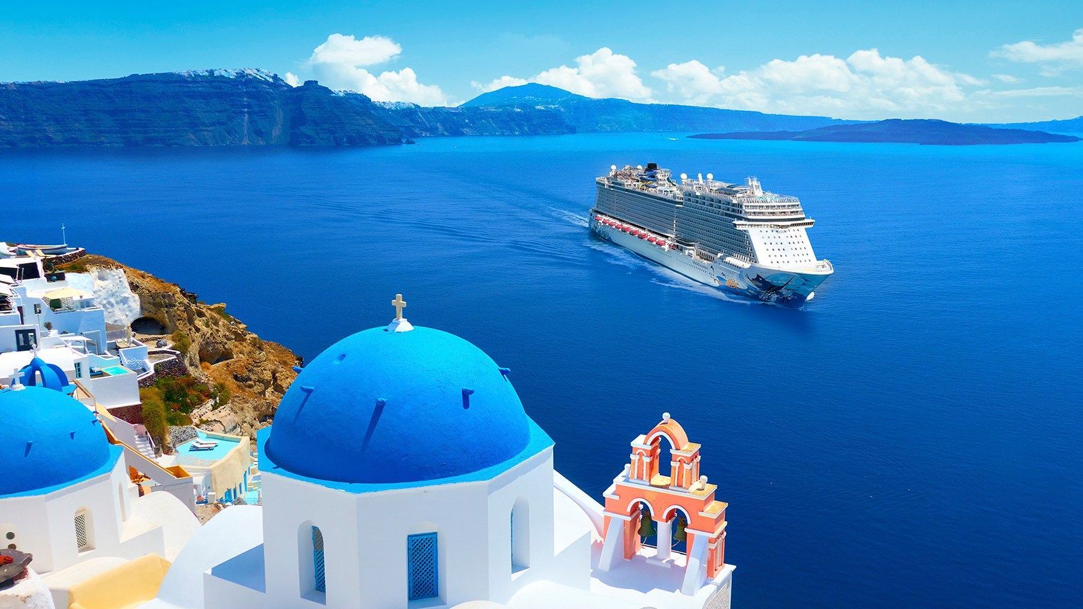 Cruise ship sailing past blue-domed buildings on a Greek island. Bright blue water and sky.