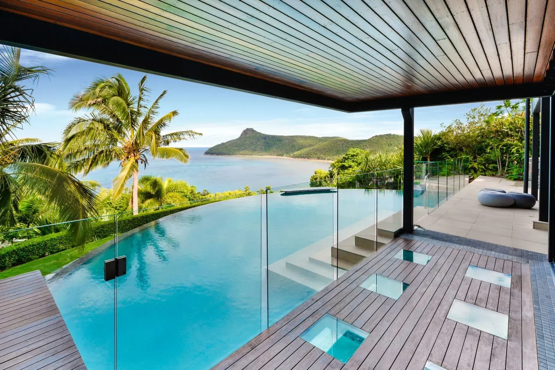 Infinity pool overlooking ocean and island, under a wood-paneled roof.