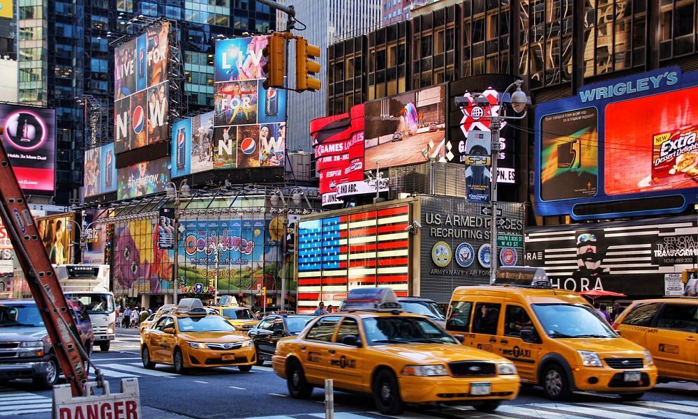 Times Square in New York City with yellow cabs, illuminated billboards, and an American flag display.