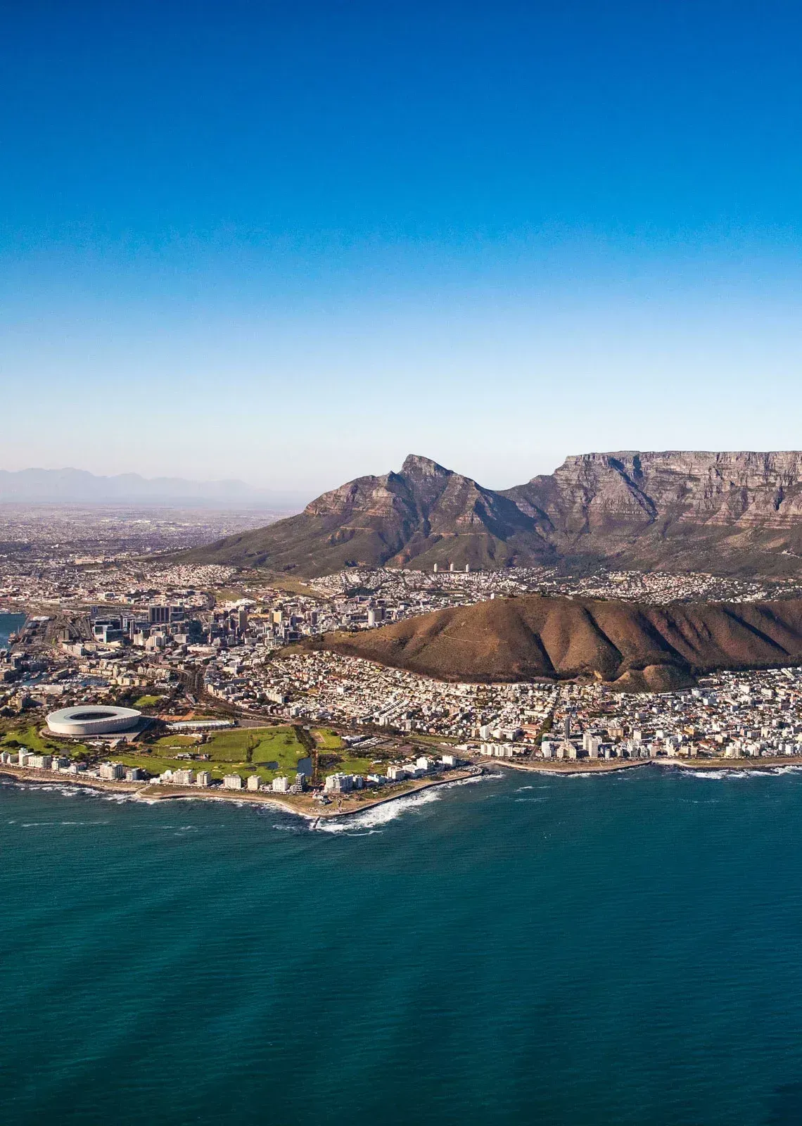 Aerial view of Cape Town, South Africa, with Table Mountain in the background and the Atlantic Ocean in the foreground.