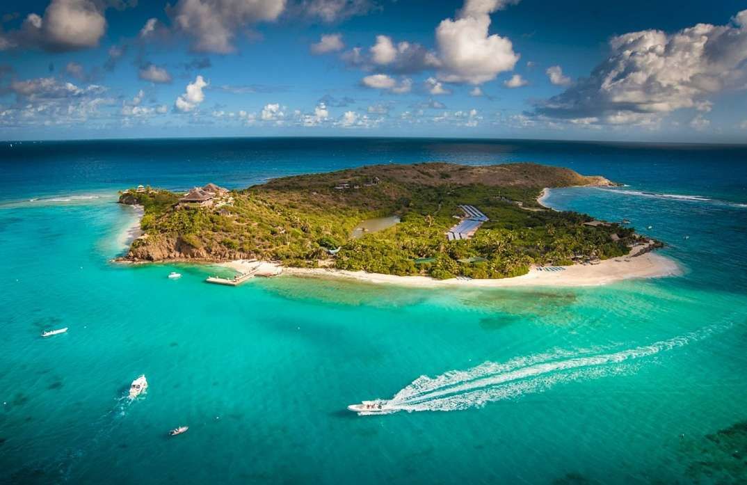 Aerial view of a lush tropical island with turquoise water, boats, and a white sand beach.