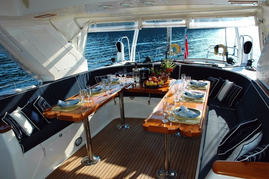 Boat interior with two wooden tables set for dining, blue cushions, and ocean view.