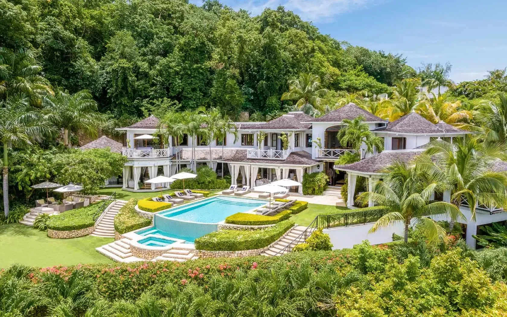 Luxurious white villa with pool surrounded by lush tropical greenery and ocean views. Round Hill Hotel and Villas, Jamaica