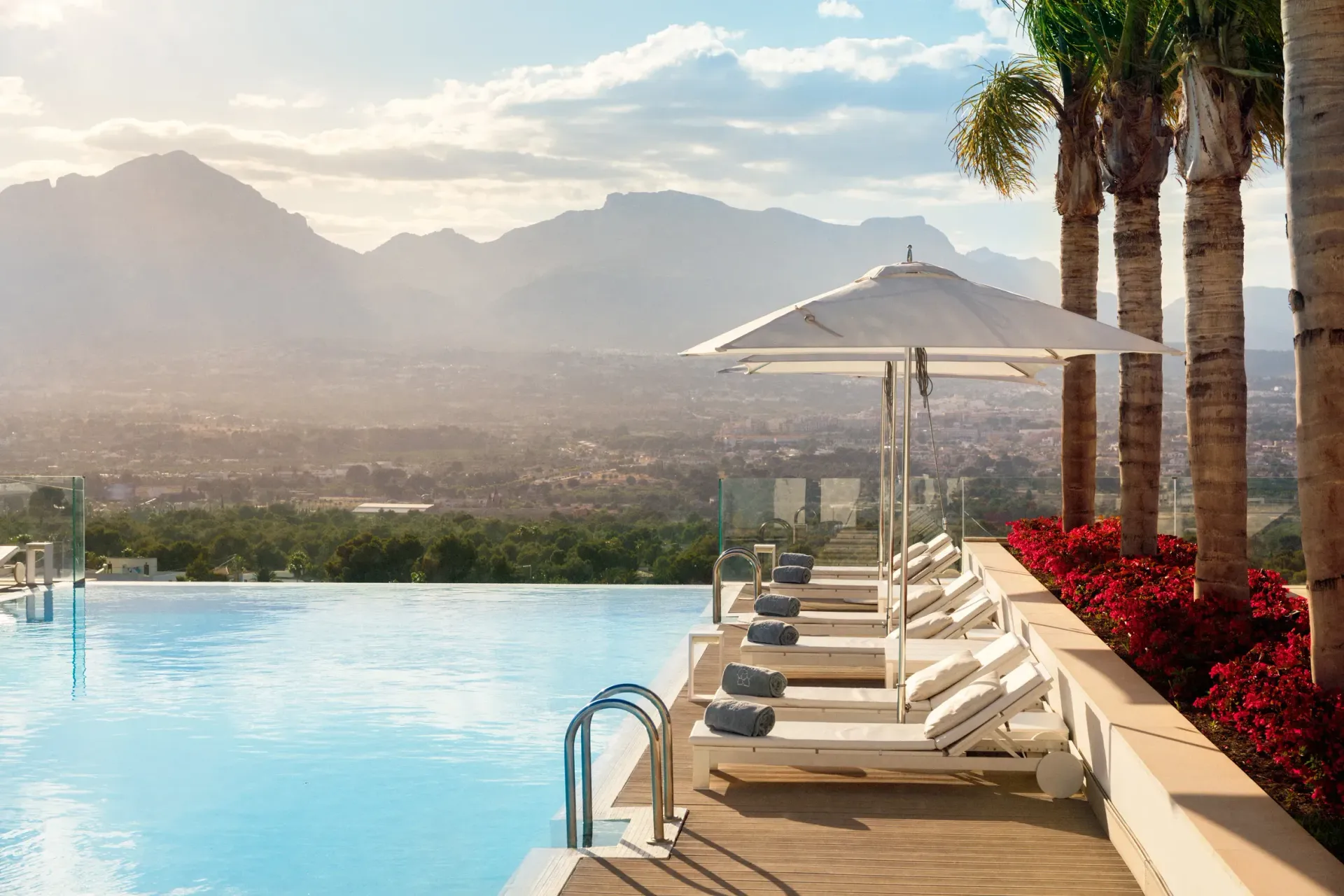 Infinity pool with mountain view, lined with white lounge chairs, under a large umbrella.
