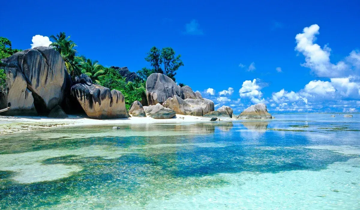 Rocky beach scene with turquoise water, blue sky, and white clouds.