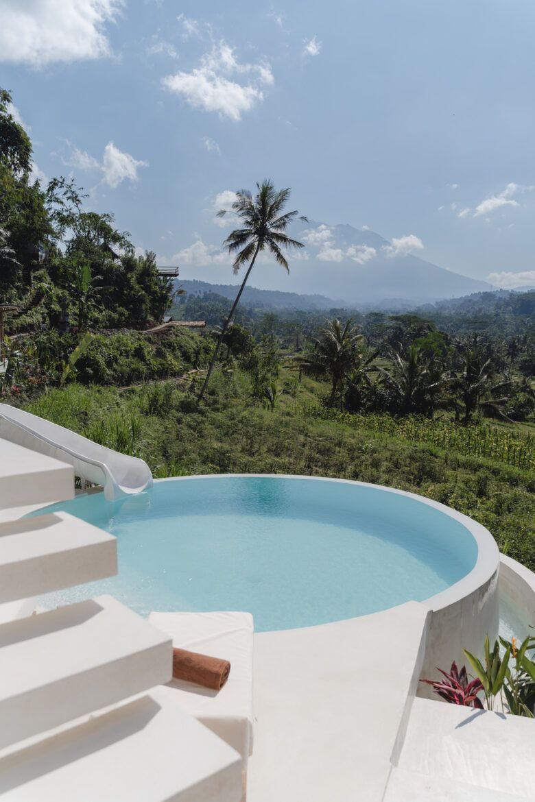 Round pool overlooking lush green valley and mountain under a sunny sky. Sidemen