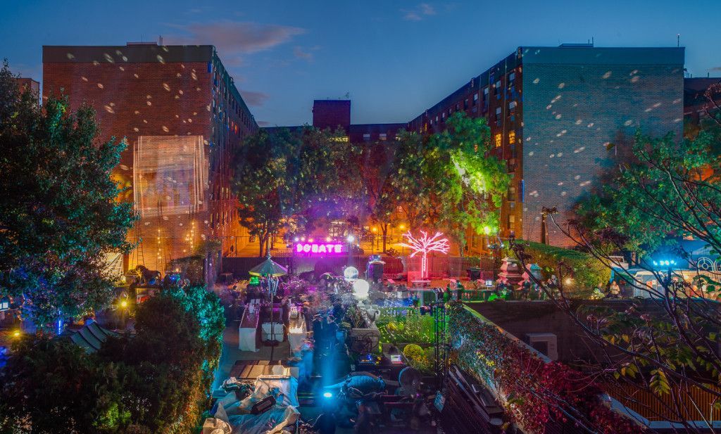 Nighttime outdoor event with illuminated buildings, trees, and a crowd of people. NYC Soho