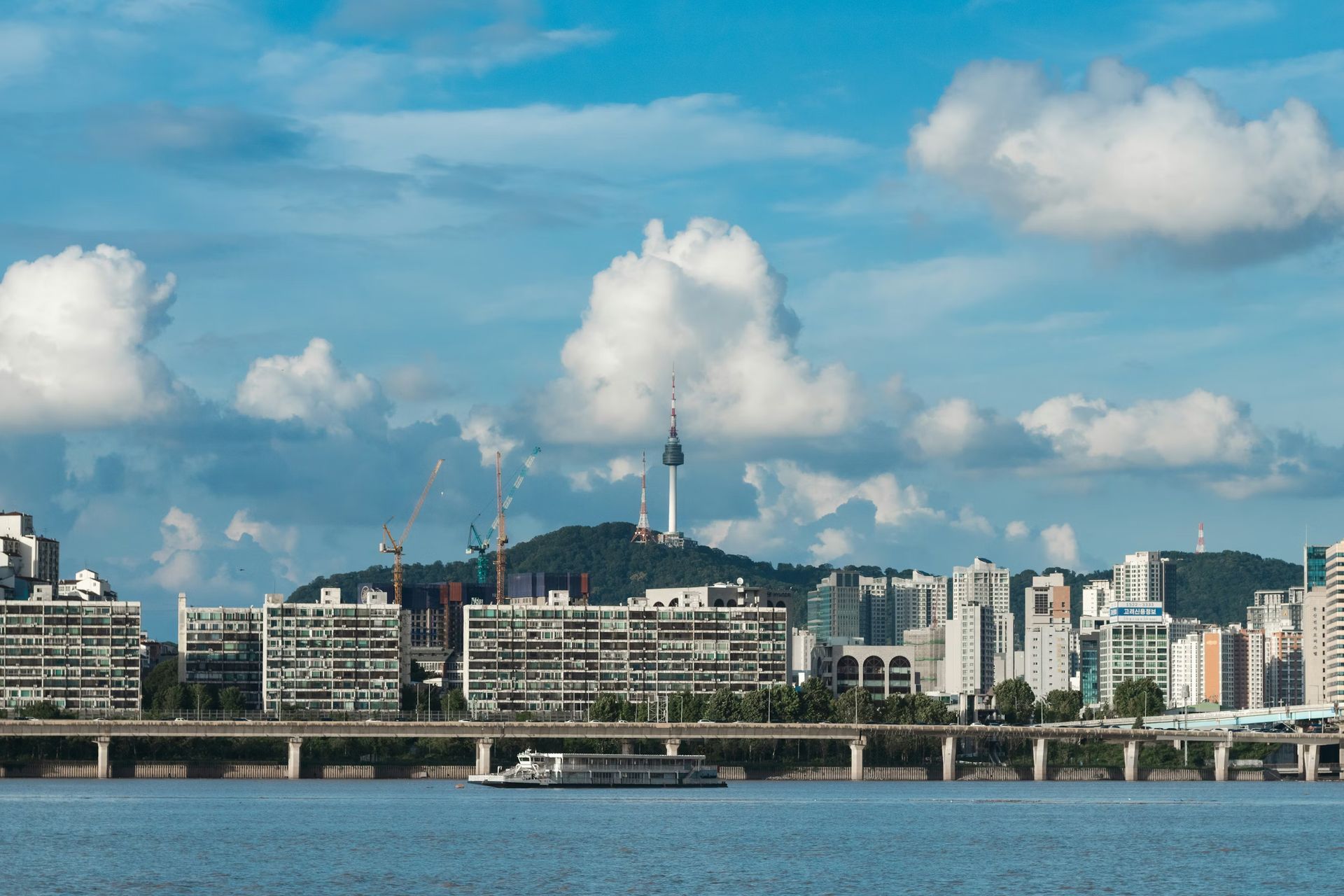 City skyline across a river under a bright blue sky with scattered clouds