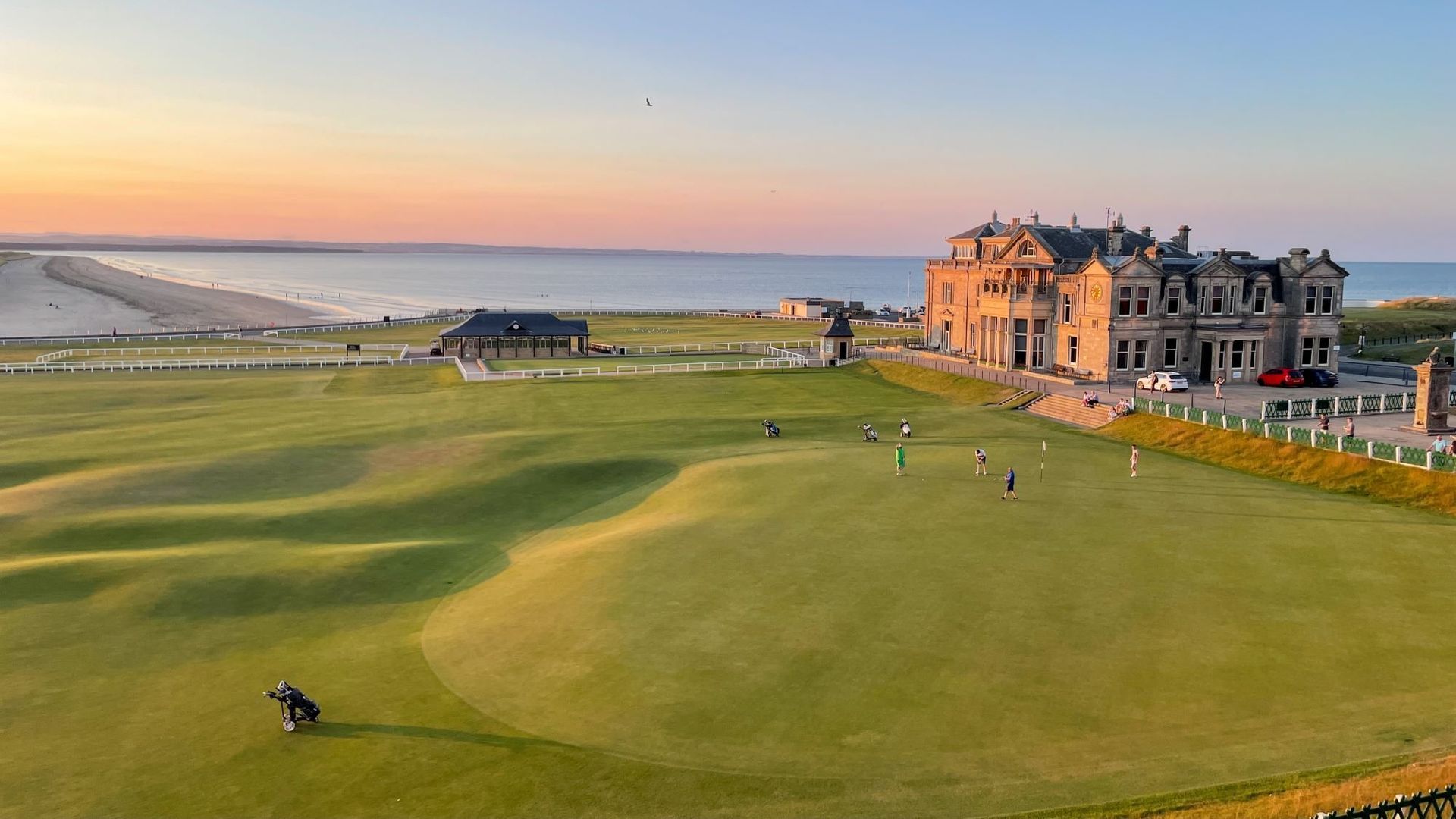 Golfers on green course near a grand castle by the ocean at sunset. St Andrews