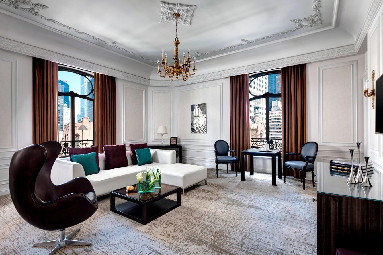 Luxurious hotel living room with white sofa, arm chair, and city views. St. Regis New York hotel suit