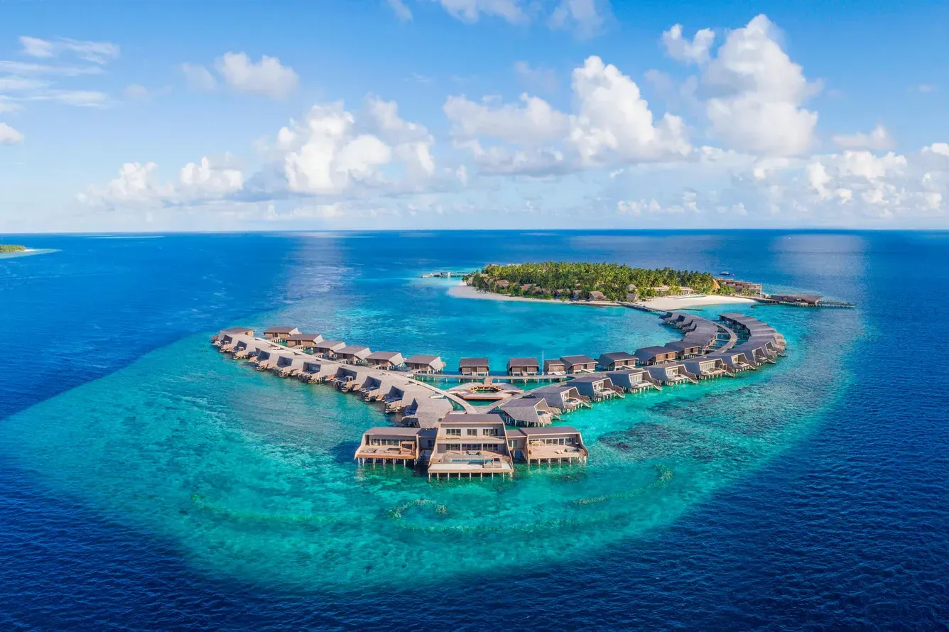 Aerial view of overwater bungalows on a tropical island in the Maldives; clear turquoise water. St Regs Maldives