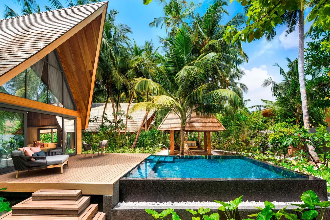 Wooden villa with pool, palm trees, and a gazebo. Luxury tropical setting.