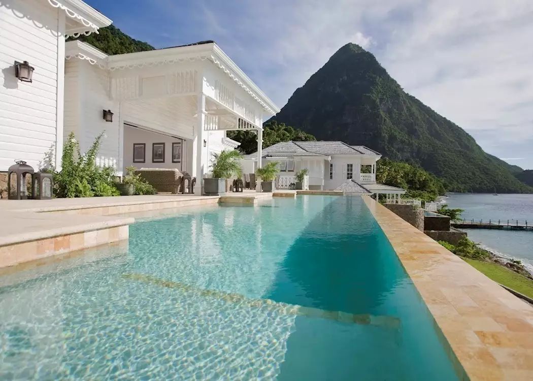 Infinity pool overlooking ocean and mountain; white buildings in background. St Lucia: Sugar Beach